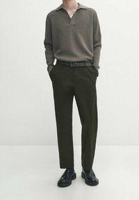 Kaki ribbet langærmet poloshirt med krave, parret med mørkegrønne bukser og sorte sko med kraftig sål.