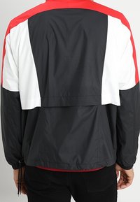 Kleur blokkerende jas met rode, zwarte en witte panelen. Lichtgewicht, soepel materiaal met een relaxte pasvorm en een verstelbare trekkoord aan de onderkant.