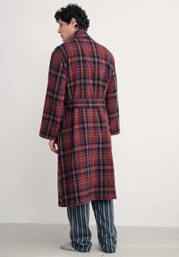 Karo bathrobe u crvenoj, plavoj i crnoj boji s dugim rukavima, pojasom u struku i bočnim džepovima. Nošen preko prugastih pidžama hlača. Mekana tekstura.