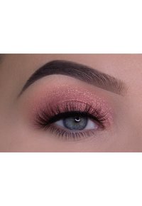 Close-up van een oog met roze glitteroogenook, lange zwarte wimpers, donkere wenkbrauwen en een natuurlijke huidtint, die een helder blauw-groene iris toont.