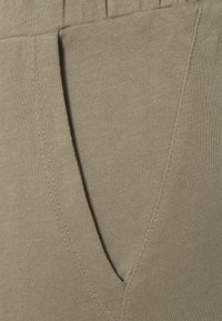 Pantalones de algodón color caqui que presentan un bolsillo lateral, una textura suave y detalles de costura visibles a lo largo de los bordes.