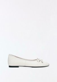 Fehér női balettcipő lekerekített orral és kis masni díszítéssel a tetején, alacsony fekete sarokkal és sima felülettel.