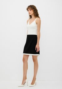 Zwarte jurk met een aansluitend witte lijfje en een uitlopende zwarte rok, met een crèmekleurige zoom. Het materiaal lijkt soepel en lichtgewicht.