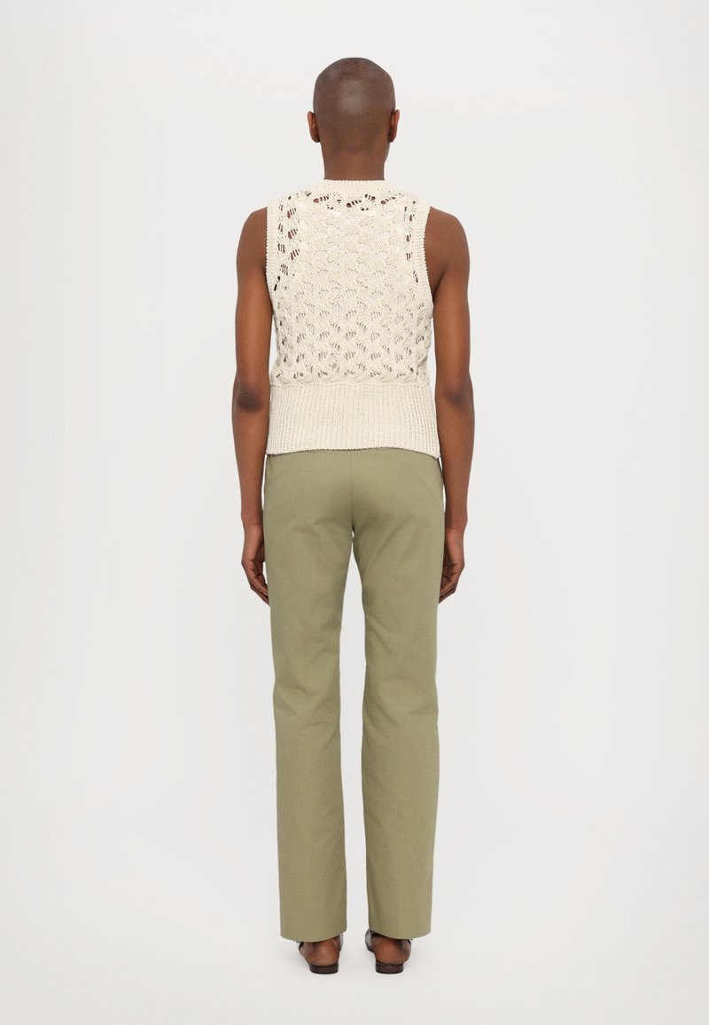 Débardeur crème en tricot avec motif ajouré et ourlet côtelé, associé à un pantalon vert ajusté. Modèle présenté de dos sur un fond neutre.