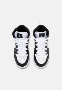 Černobílé tenisky s klasikou nízkou siluetou. Mají perforovanou špičku, bílé tkaničky a zelený akcent ve tvaru loga na jazyku.