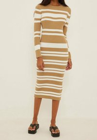 Vestido midi acanalado en color beige con rayas horizontales blancas, con mangas largas y una silueta ajustada. Combinado con sandalias de plataforma negras.