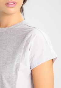 Szara i biała koszulka z krótkim rękawem o kontrastujących kolorach; miękki materiał, okrągły dekolt i mankiety. Prosty design, bez wzorów.