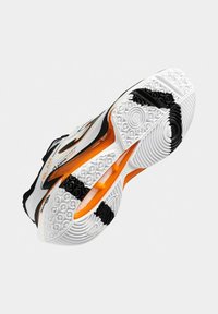 Zapatilla deportiva blanca con acentos en negro y naranja, que cuenta con una suela de goma texturizada, patrones redondos y un diseño reforzado para mayor soporte.