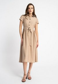 Beżowa sukienka na guziki z krótkimi rękawami, paskiem w talii i zwiewnym dołem. Teksturowany materiał i długość do kolan. Podkreślona guzikami.