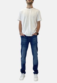Camiseta de algodón blanca, jeans de denim azul con un ligero desgaste, y zapatillas blancas. Diseño simple, corte regular y detalles de costura sutiles.