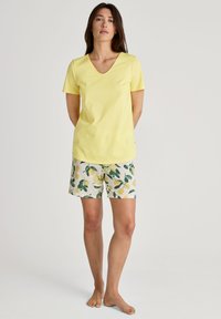 Gelbes Baumwoll-V-Ausschnitt-T-Shirt kombiniert mit kurzen Hosen mit Zitronenmuster in Weiß und Grün. Das Outfit hat kurze Ärmel und eine lockere Passform.