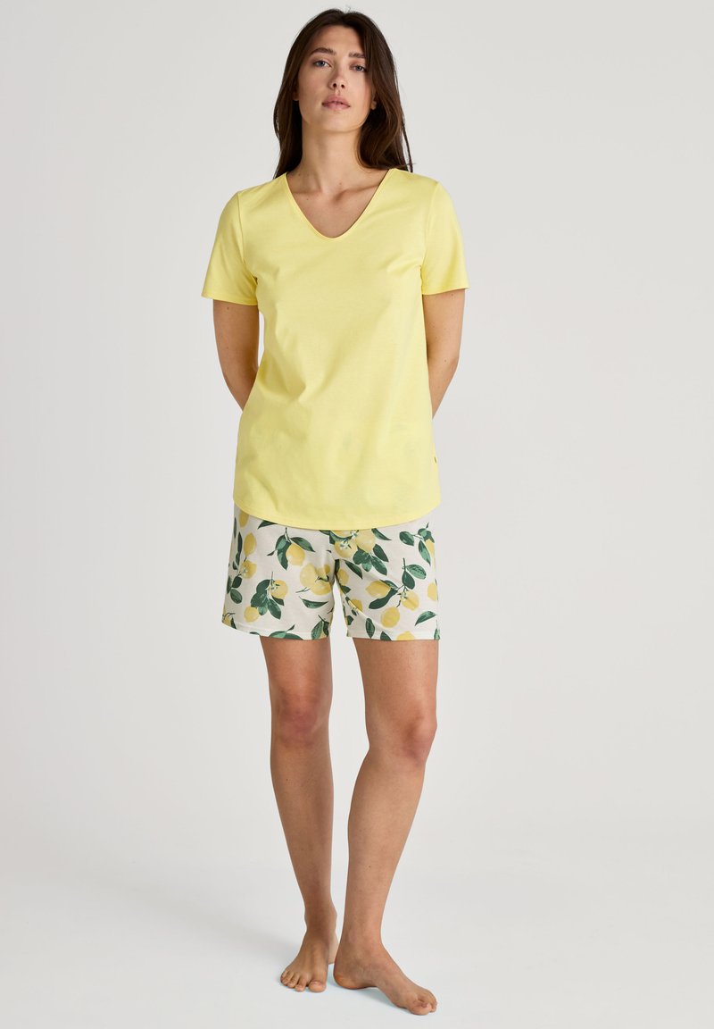 Gelbes Baumwoll-V-Ausschnitt-T-Shirt kombiniert mit kurzen Hosen mit Zitronenmuster in Weiß und Grün. Das Outfit hat kurze Ärmel und eine lockere Passform.