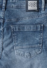 Blå denimjeans med ett bakfickor som har dubbelsydda sömmar och en etikett som säger "COLOR MOOD CECIL." Mjuk textur och urtvättad look.