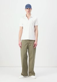 Witte polo met korte mouwen gecombineerd met olijfgroene wijde broek en witte sneakers. De persoon draagt een blauwe pet.