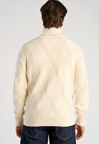 Roomkleurige trui met een gestructureerd ruitpatroon, hoge kraag en geribde zoom en manchetten, ontworpen voor een aansluitende pasvorm.