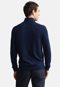 Marineblauwe pullover gemaakt van gladde stof, met een hoge kraag en lange mouwen. De achterkant is eenvoudig ontworpen met een geribde zoom.