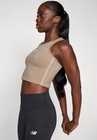 Beige avkortet tanktop med slim fit, med subtile side sømmer, båret med høydejusterte svarte leggings med logo.