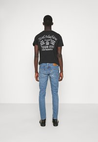 Svart kortärmad T-shirt med vit text och grafik på baksidan, i kombination med ljusblå denimjeans och svarta skor. Enkel, åtsittande design.
