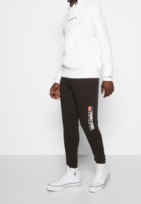 Vit huvtröja med logotyp fram, svarta sweatpants med sidologotyptryck och vita högskor med svarta accenter.