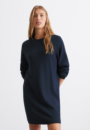 Navy blue dzianinowa sukienka o luźnym kroju, okrągłym dekolcie i długich rękawach. Miękka tekstura, do kolan długość, bez widocznych wzorów.