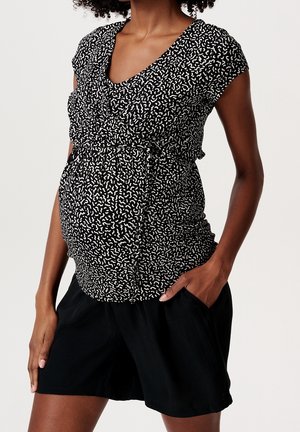 Tunika ciążowa w czarno-białym abstrakcyjnym wzorze, z dekoltem w serek, krótkimi rękawami i marszczeniami. W zestawie z czarnymi szortami.