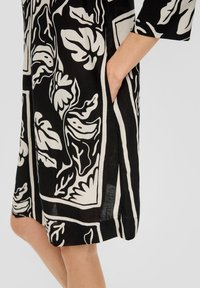 Robe noire et blanche avec des motifs floraux, manches trois-quarts et poches latérales ; fabriquée en tissu léger avec une coupe décontractée.