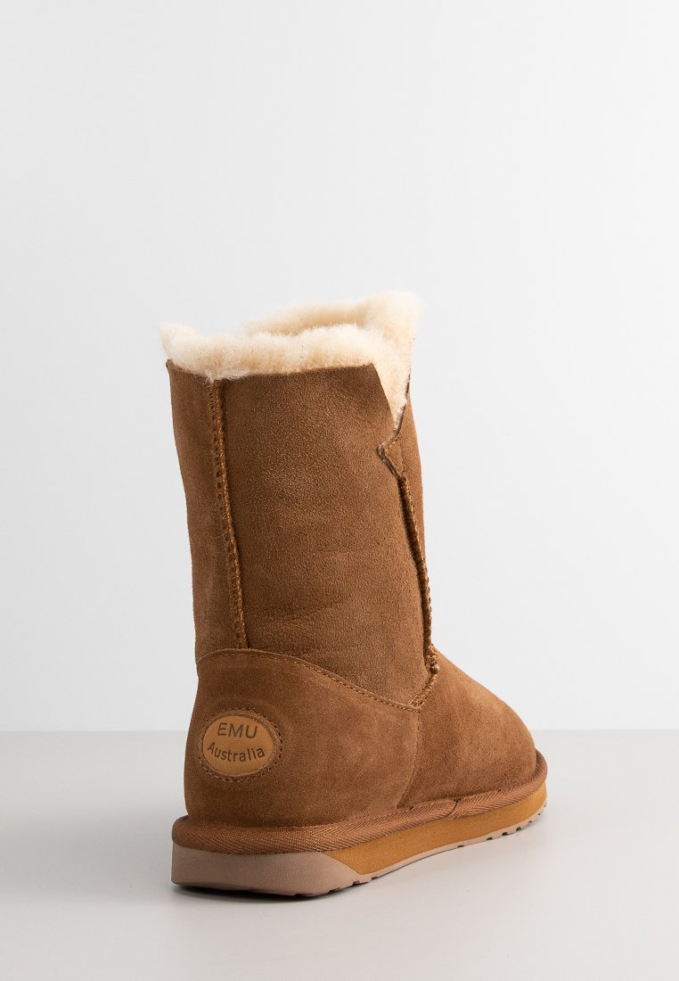 Braune Wildleder-Stiefelette mit einem flauschigen cremefarbenen Futter, flacher Sohle und einem runden Logo-Patch an der Ferse. Sanfte Textur und schlichtes Design.