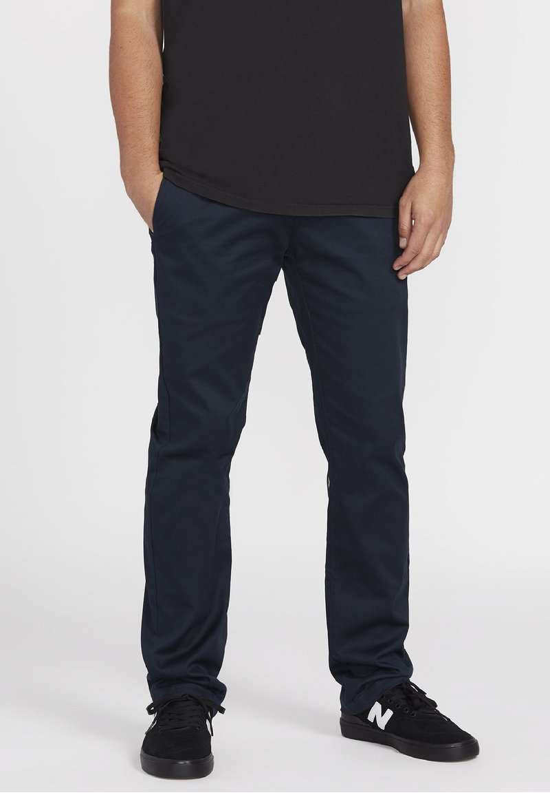 Pantalons bleu marine à coupe ajustée en tissu mélangé de coton. Dotés de poches avant et d'une texture lisse, associés à des sneakers noires.