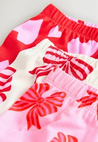 Trzy pary spodni z elastycznym pasem: czerwone w różowe serca, kremowe w czerwone paski i różowe z czerwonymi wzorami kwiatowymi. Miękka tkanina, swobodny design.