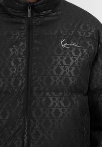 Giacca puffa nera con motivo logo tono su tono in tutta la superficie, dotata di chiusura con zip e di una prominente firma bianca sul petto.
