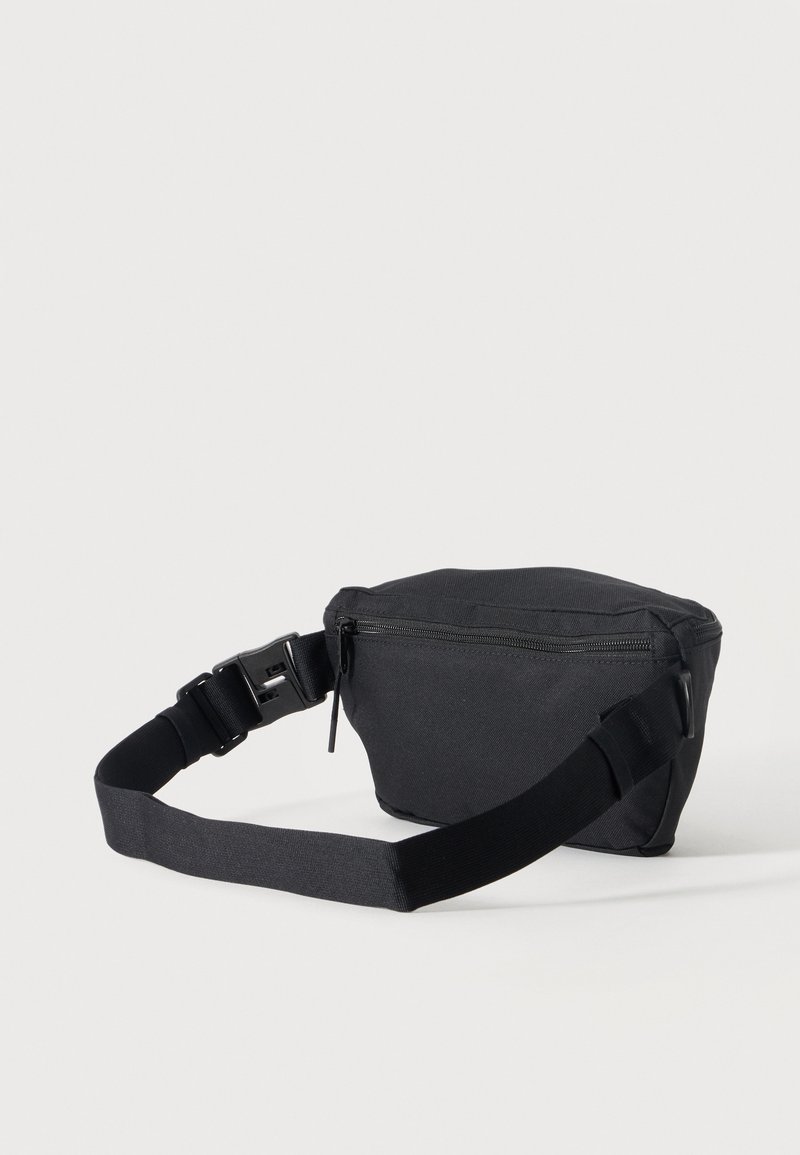 Small black fabric waist bag with zipper closure and adjustable strap with plastic buckle on plain background.