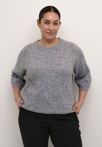 Grijze gebreide trui met een textuur kabelpatroon, brede ribbels rond de hals, en driekwart mouwen, gecombineerd met donkere broek.