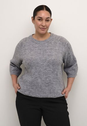 Hallatud hall kampsun tekstuurse kaablipatterniga, lai ribidega ümar kaelus ja kolmveerandvarrukad, koos tumedate pükstega.