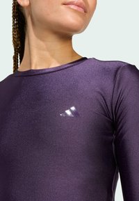 Purple athletic top with a glossy texture. Features a round neckline and three white stripes logo on the left chest area.