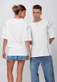 White oversized t-shirts featuring black side seams, paired with denim shorts (frayed hem) and jeans. Smooth fabric texture.