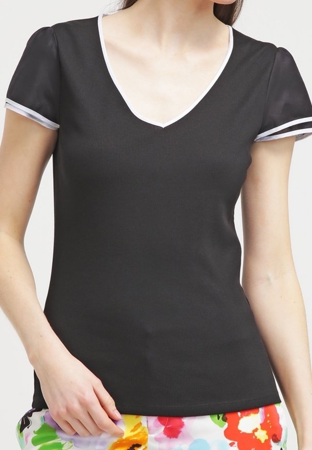 Woman wearing a black short-sleeve top with white trim and colorful floral-patterned pants, hand resting at her side.