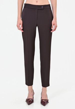 Pantaloni neri slim fit con vita alta e chiusura con bottoni, indossati con décolleté a punta color bordeaux scuro con fiocchi.