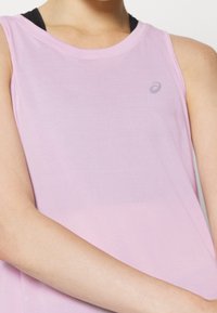 Vaaleanpunainen hihaton urheilupaita, joka on valmistettu pehmeästä kankaasta. Paidassa on pyöreä pääntie ja pieni logo korostus rinnassa.