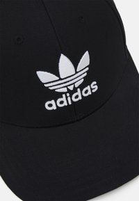 Svart baseballkeps i tyg med en vit broderad Adidas-logotyp och trefoil-design på framsidan. Krökt skärm, enfärgad.