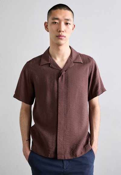Short-sleeve, button-up shirt in textured dark brown fabric. Features a camp collar and a relaxed fit, with a single button closure.