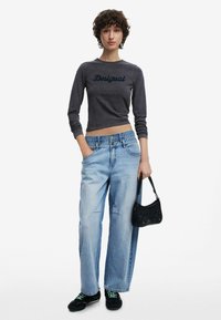 Top corto a maniche lunghe grigio scuro con logo "Desigual", abbinato a jeans baggy azzurri e sneaker nere. Piccola borsa nera con tracolla.