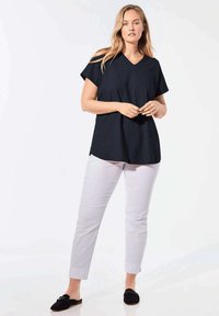 Marineblaues V-Ausschnitt-T-Shirt mit kurzen Ärmeln, kombiniert mit hellgrauen Slim-Fit-Hosen und schwarzen Slippern. Geschmeidiger Stoff, lässige Passform.
