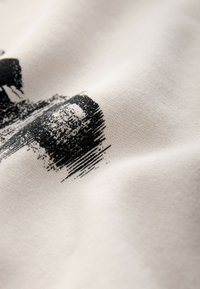 Gros plan sur un tissu blanc avec un imprimé graphique noir texturé présentant des formes rectangulaires de style coup de pinceau.