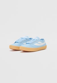 Light blue canvas sneakers with white stripes, featuring rounded toes and ribbed gum soles. Laces through metal eyelets complete the design.