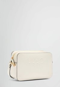 Sac crossbody blanc en carré fabriqué en matériau texturé, avec une fermeture éclair dorée, un logo embossé et un bord noir sur les arêtes.