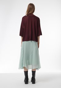 Bourgondische gebreide top met korte mouwen, gecombineerd met een lichtgroene asymmetrische rok; zwarte kniehoge laarzen maken de outfit compleet.