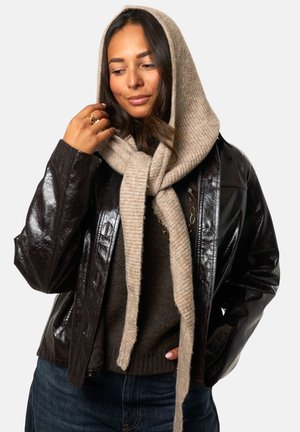 Veste en cuir marron avec une finition brillante, pull gris en dessous, et une écharpe en laine beige, texturée, nouée lâchement autour du cou.