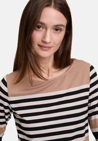 Langarmoberteil mit einem gestreiften Muster. Der obere Teil ist beige; der untere Teil hat abwechselnd schwarze und hautfarbene Streifen. Die Stoffstruktur ist weich.