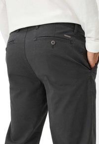 I pantaloni in cotone neri presentano una texture liscia, due tasche posteriori con bottoni e un discreto marchio sul cinturino.