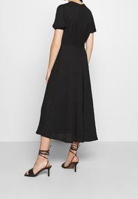 Vestido midi negro con mangas cortas abullonadas, tejido texturizado, falda acampanada y cremallera trasera. Combinado con sandalias de tacón negro con tiras.